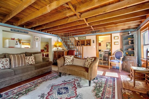 Cozy living room with wooden beams, a patterned rug, comfortable seating, and a view of a dining area.