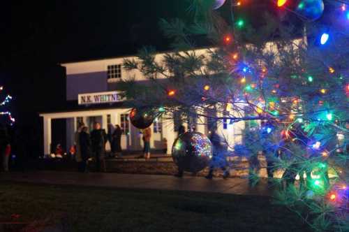 A festive scene at night with colorful Christmas lights and people gathered near a decorated building.