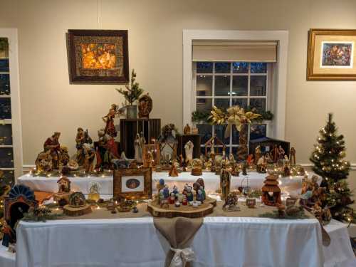 A festive display of nativity scenes and decorations on a table, with lights and holiday decor in a cozy room.