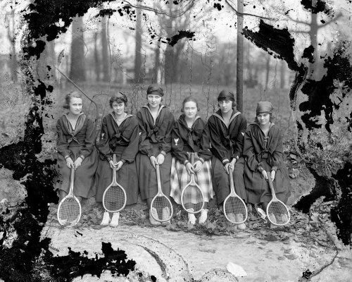 A group of seven young women in matching outfits, each holding a tennis racket, posed outdoors.