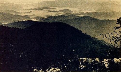 A misty mountain landscape with layered hills and valleys, captured in a vintage black-and-white style.