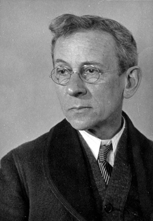 Black and white portrait of a man with glasses, wearing a suit and tie, looking thoughtfully to the side.