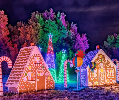 Colorful gingerbread houses and a lit tree surrounded by candy canes, set against a night sky.