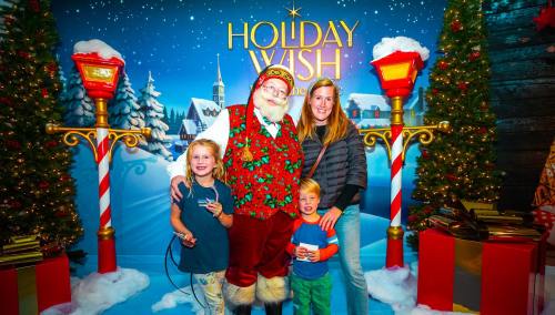 A family poses with Santa Claus in a festive setting, surrounded by holiday decorations and a snowy backdrop.