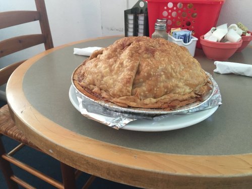 A large, golden-brown pie sits on a plate on a table, with a rustic wooden chair in the background.