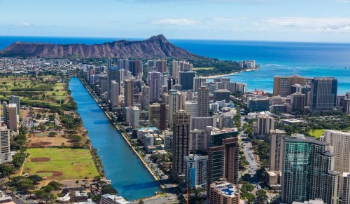 Aerial view of a city skyline with a river, parks, and Diamond Head in the background, showcasing a coastal landscape.