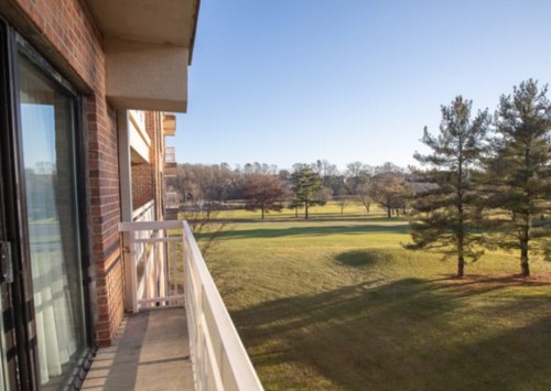 A balcony view overlooking a green lawn and trees under a clear blue sky.