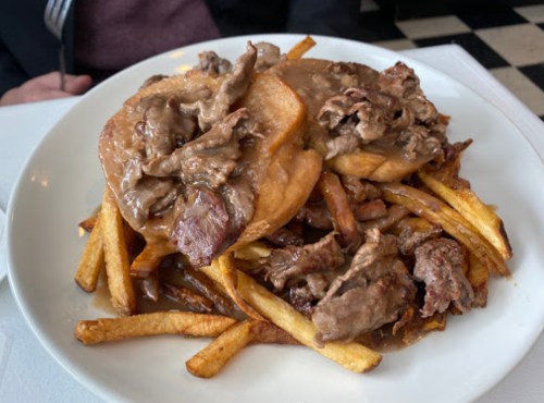 A plate of fries topped with two pieces of bread and beef smothered in gravy.