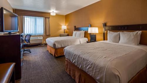 A cozy hotel room featuring two beds, a desk, a TV, and warm lighting.