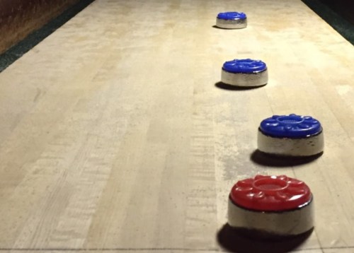 Four curling stones, two red and two blue, positioned on a wooden curling rink.