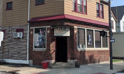 A corner building with a sign reading "Hotel Cafe" and large windows, featuring a brick and siding exterior.