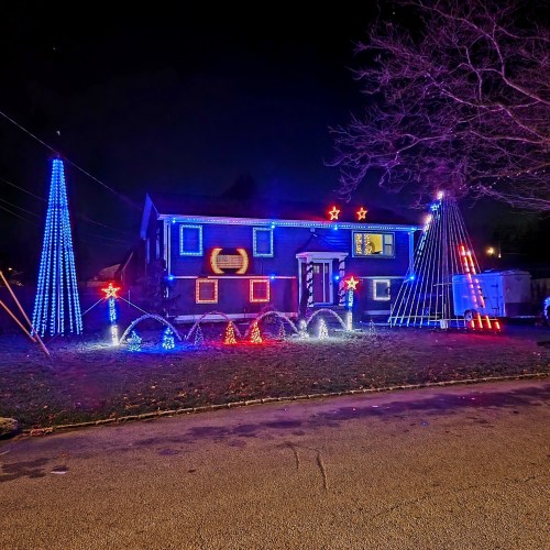 A house decorated with colorful Christmas lights, featuring blue and red trees and star-shaped decorations in the yard.
