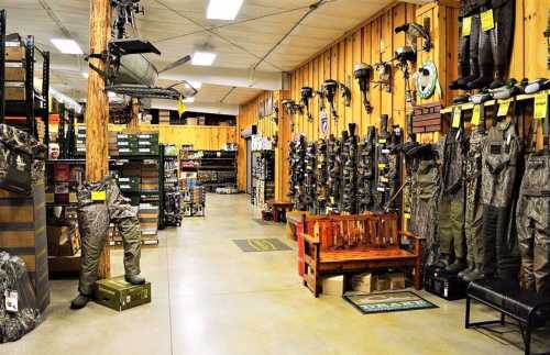 A spacious store aisle displaying hunting gear, camouflage clothing, and outdoor equipment on wooden shelves.