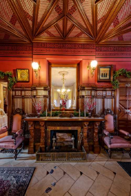 Elegant room featuring a wooden ceiling, ornate fireplace, and plush chairs, decorated with greenery and warm lighting.