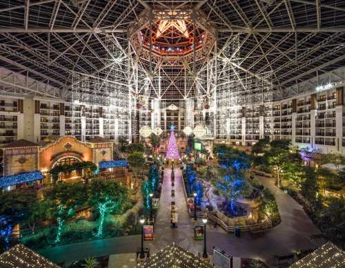 A spacious indoor atrium with a tall glass ceiling, decorated with colorful lights and a large Christmas tree.