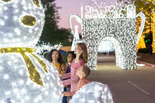 A group of children and adults admire festive light displays, including a large snowman, during a holiday event.