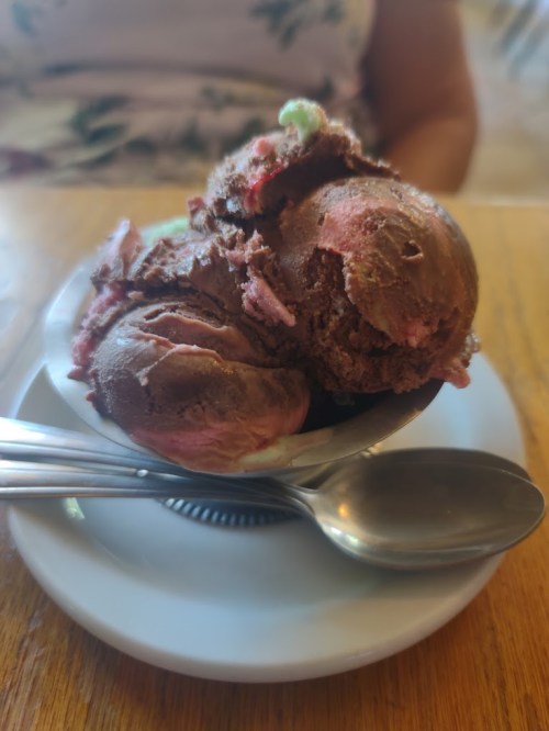 A bowl of chocolate and strawberry ice cream with two spoons on a wooden table.