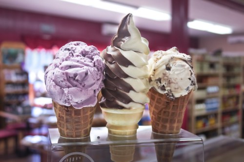 Three ice cream cones with purple, chocolate, and vanilla swirls, displayed in a shop with a cozy interior.