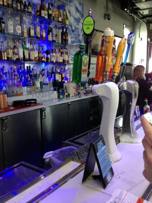 A bar with a variety of liquor bottles on shelves and several beer taps, including a Patron tequila tap.