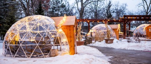 Cozy igloos with string lights in a snowy outdoor setting, surrounded by trees and wooden structures.