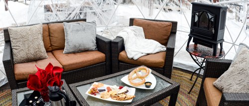 Cozy indoor seating with plush cushions, a small table with snacks, and a heater, set in a snowy outdoor environment.
