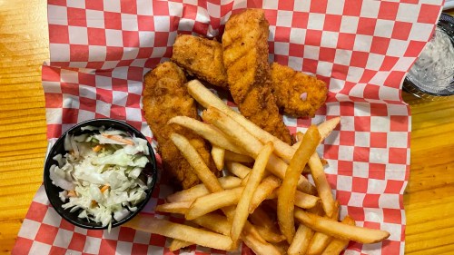 A plate of fried chicken tenders, French fries, and a side of coleslaw on a red and white checkered paper.