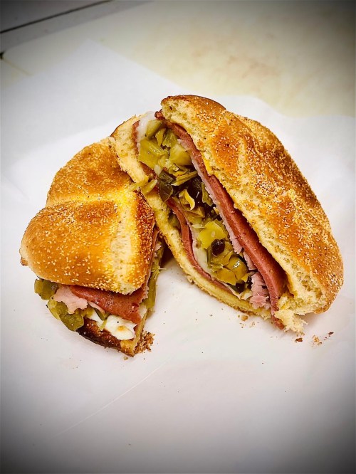 A sandwich cut in half, filled with layers of meat, pickles, and mustard, on a toasted bun.