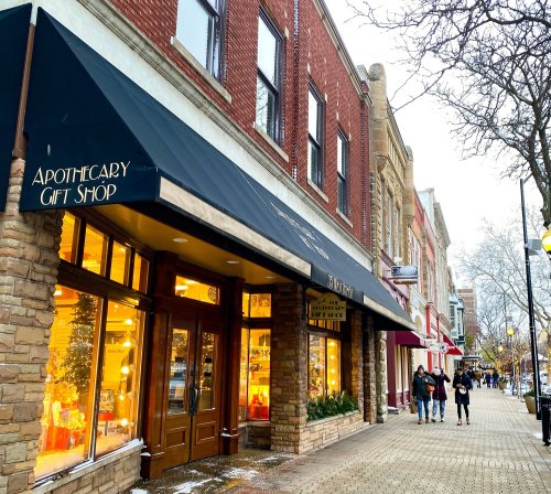 A charming street scene featuring a gift shop with a black awning, surrounded by brick buildings and pedestrians.