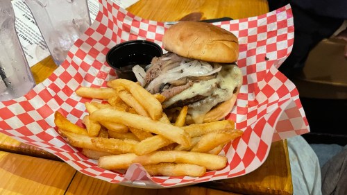 A juicy burger with melted cheese and onions, served with a side of golden French fries in a checkered basket.