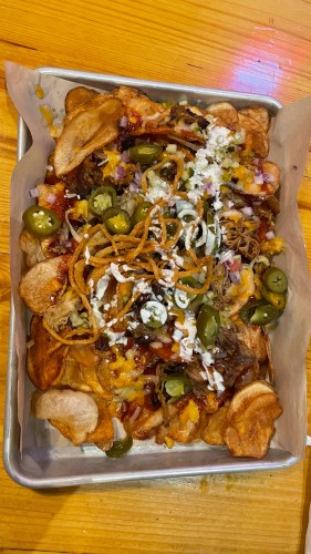 A tray of loaded nachos topped with cheese, jalapeños, onions, and crispy onions on a bed of potato chips.