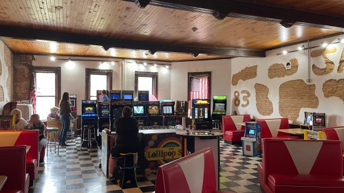 A retro arcade with colorful booths, vintage games, and a lively atmosphere, featuring people enjoying the space.