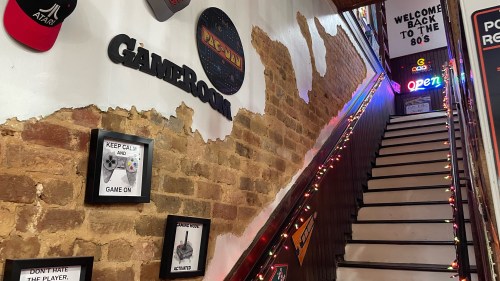 A staircase leading to a retro-themed gamer room, decorated with vintage gaming signs and colorful lights.