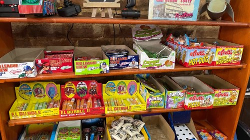 A wooden shelf filled with colorful vintage candy boxes and toys, featuring various nostalgic treats and snacks.