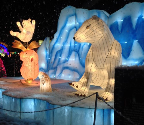 Illuminated ice sculptures of polar bears and other animals against a snowy backdrop, creating a festive winter scene.