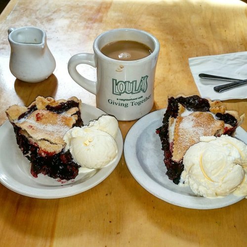 Two slices of berry pie with scoops of vanilla ice cream, accompanied by a cup of coffee on a wooden table.