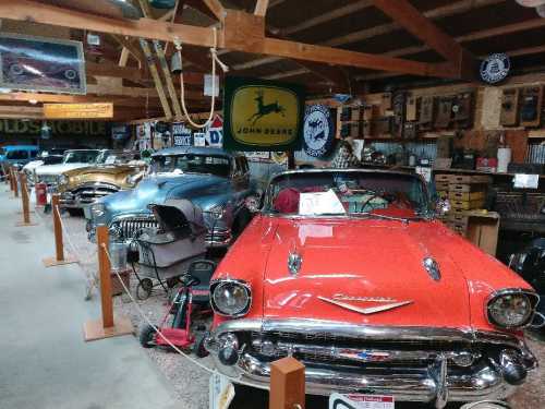 A collection of vintage cars displayed in a rustic garage, featuring a bright red 1957 Chevrolet in the foreground.