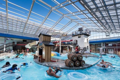 Indoor water park scene with a lighthouse, water slides, and guests floating in tubes in a blue pool.