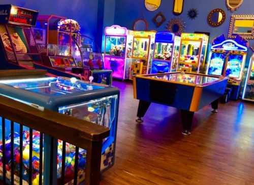 A vibrant arcade filled with colorful games, including skee-ball and claw machines, under bright lights.