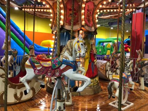 A colorful carousel with ornate horses, surrounded by vibrant inflatable attractions in a playful indoor setting.