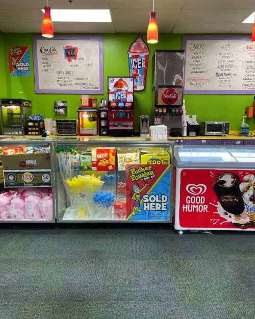 A colorful snack counter featuring ice cream, drinks, and various snacks in a vibrant green setting.