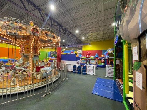 Indoor amusement area featuring a carousel, inflatable attractions, and colorful play structures.