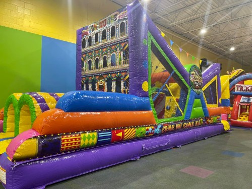 A colorful inflatable bounce house with various sections, including slides and obstacles, in a play area.