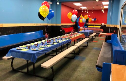 A colorful party room with decorated tables, balloons, and seating, ready for a celebration.