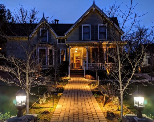A charming house illuminated at night, with a brick pathway and decorative lights outlining the trees and porch.