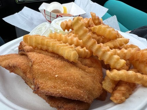 A plate of crispy fried fish fillets with crinkle-cut fries and dipping sauces on the side.