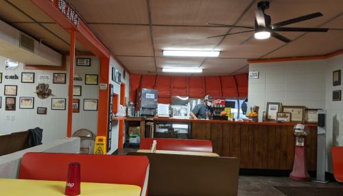 A cozy diner interior with a counter, a cook in the kitchen, and vintage decor on the walls.