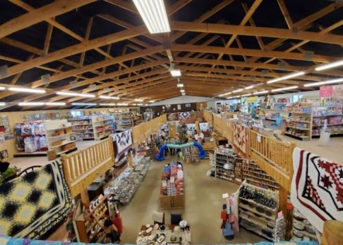 A spacious store interior with wooden beams, shelves filled with various products, and colorful quilts displayed.