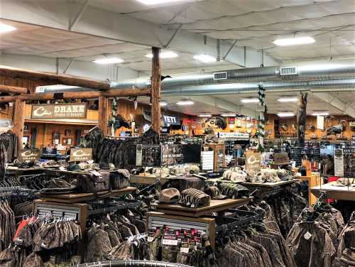 A spacious retail store filled with hunting apparel, hats, and outdoor gear, featuring wooden decor and various brands.