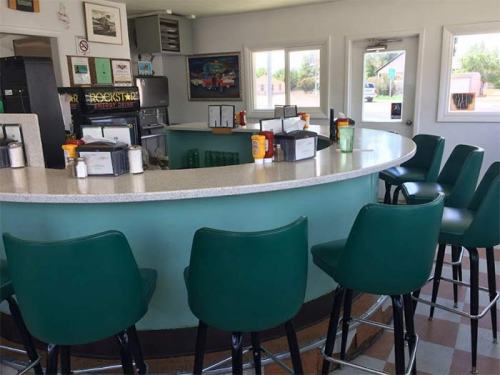 A retro diner interior featuring a curved counter with green stools and large windows, creating a bright atmosphere.