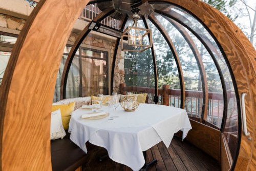 A cozy outdoor dining pod with a wooden frame, a table set for two, and a lantern hanging above.